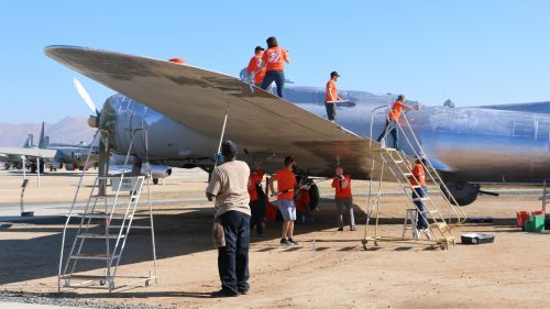 People repairing an aircraft wing outdoors with tools and ladders.
