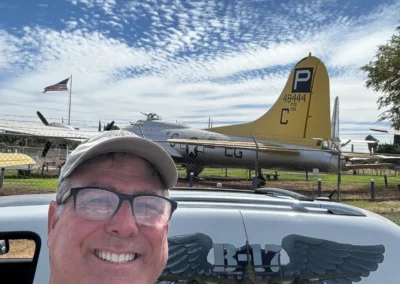 Man smiling near vintage airplane under cloudy sky.